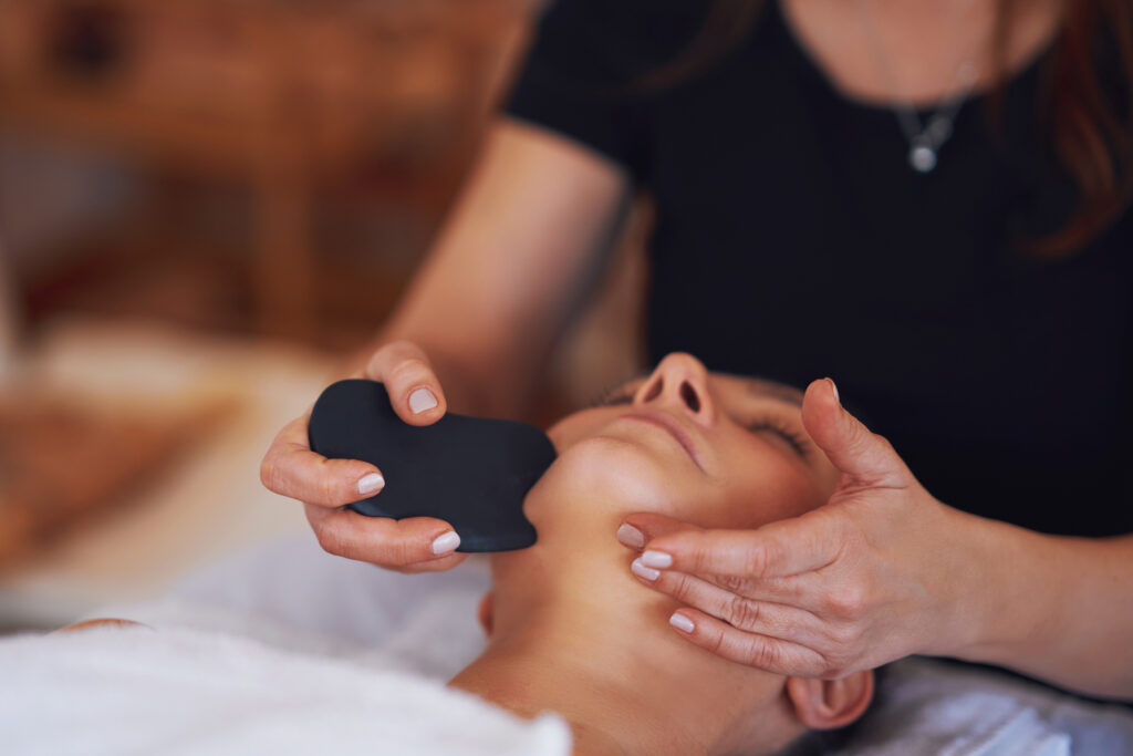 A brunette woman enjoys Gua Sha massage on her face for gua-sha-and-massage blog.